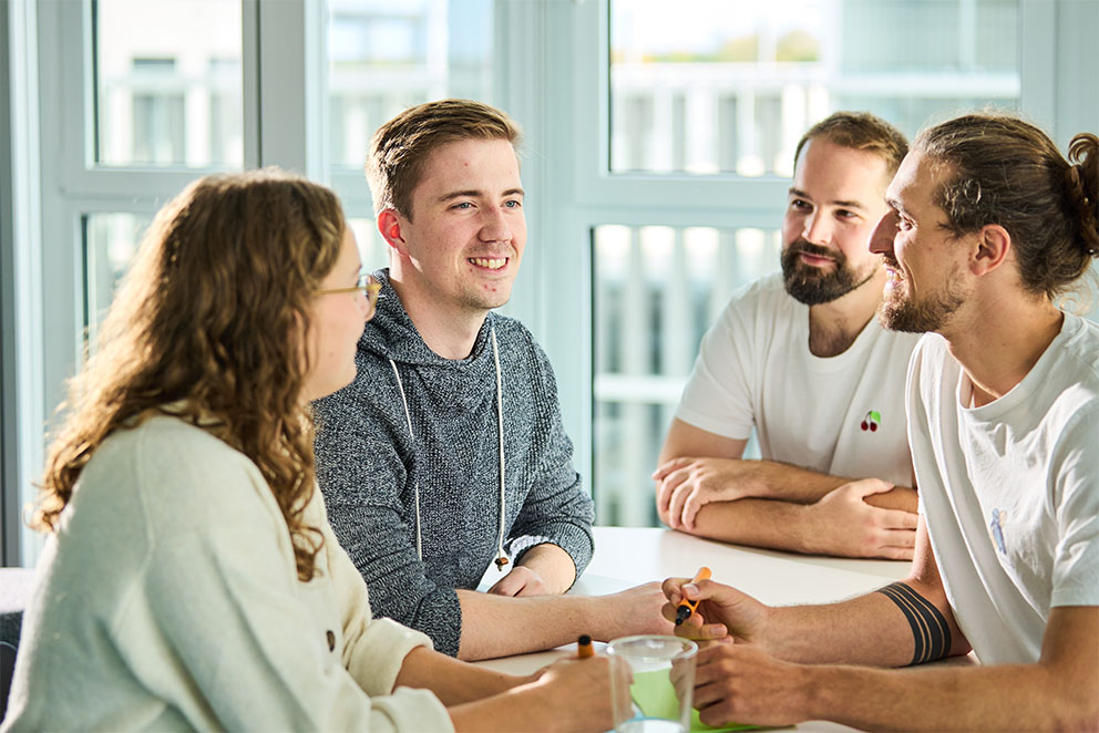 4 Kolleg*innen sitzen am Tisch und besprechen sich